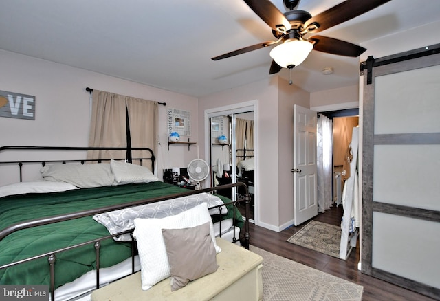 bedroom with a barn door, baseboards, dark wood finished floors, ceiling fan, and a closet