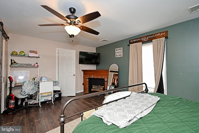 bedroom featuring a brick fireplace, ceiling fan, visible vents, and dark wood finished floors