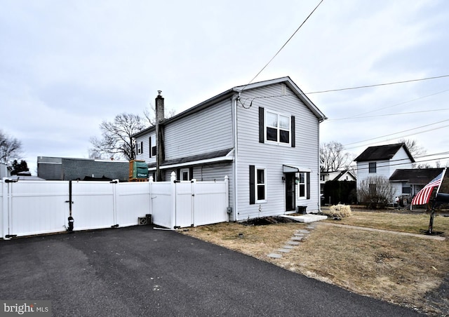 view of front facade with a chimney, fence, and aphalt driveway