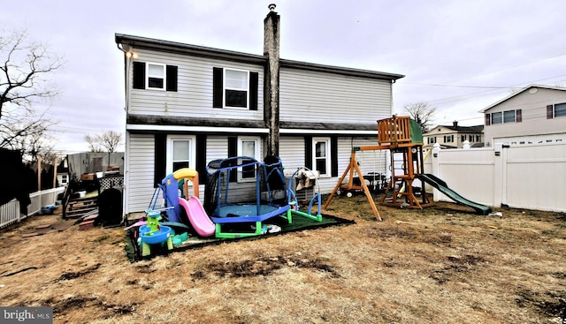 rear view of property featuring a trampoline, a playground, and fence