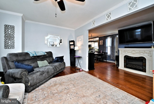 living room featuring dark wood-style floors, a premium fireplace, a ceiling fan, ornamental molding, and baseboards