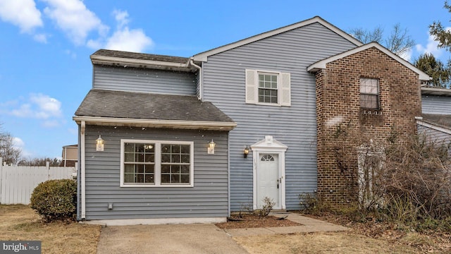 traditional-style home featuring a shingled roof, brick siding, and fence