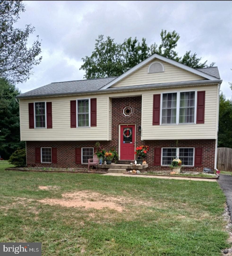 raised ranch featuring entry steps, a front lawn, and brick siding