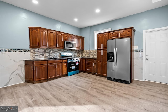 kitchen with light wood-type flooring, dark stone countertops, appliances with stainless steel finishes, and a sink