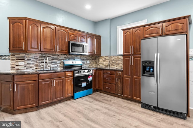 kitchen with light wood finished floors, tasteful backsplash, dark stone countertops, stainless steel appliances, and a sink