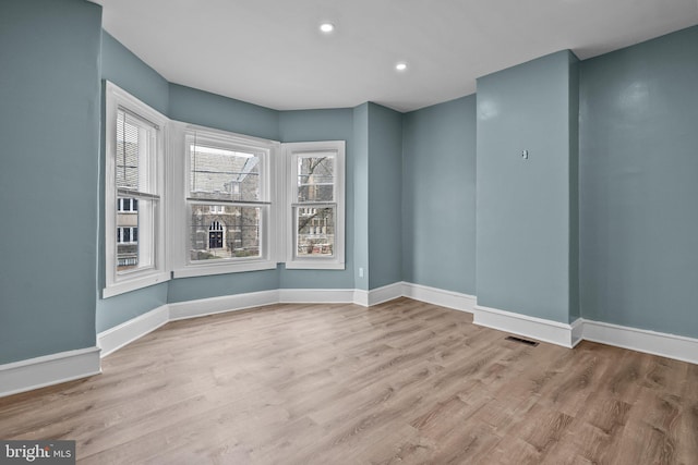 spare room with light wood-type flooring, visible vents, and baseboards