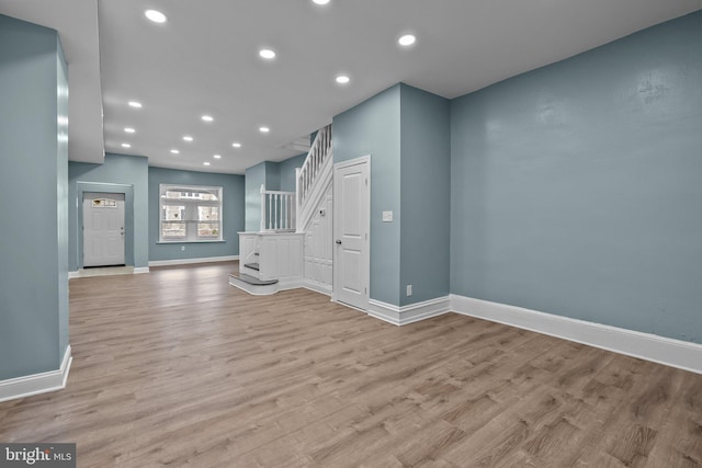 unfurnished living room featuring light wood-style floors, baseboards, stairway, and recessed lighting