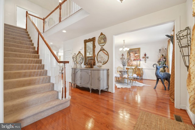 entrance foyer with wood-type flooring, visible vents, stairway, a chandelier, and baseboards