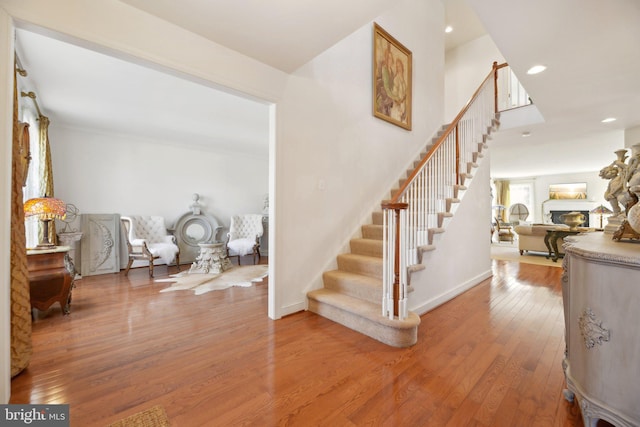 stairway with a lit fireplace, hardwood / wood-style floors, recessed lighting, and baseboards