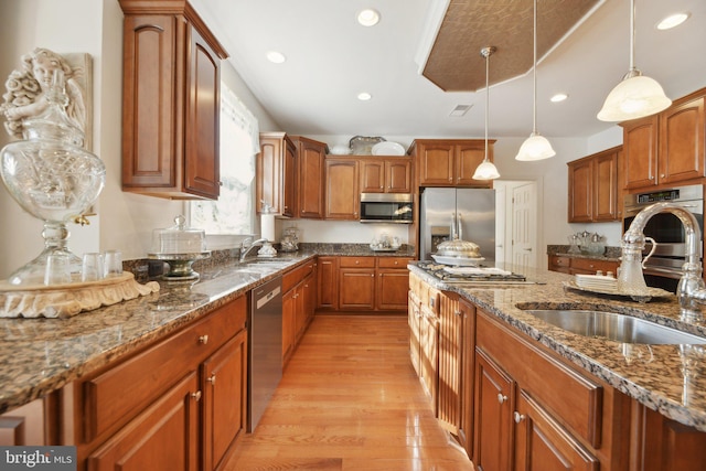 kitchen with stainless steel appliances, dark stone countertops, hanging light fixtures, and a sink