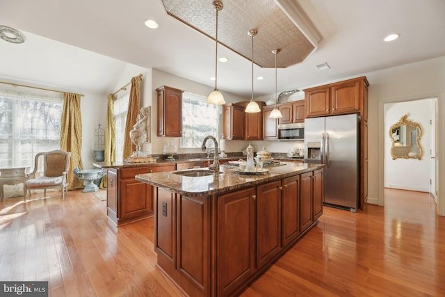 kitchen featuring a center island with sink, appliances with stainless steel finishes, hanging light fixtures, light wood-type flooring, and a sink