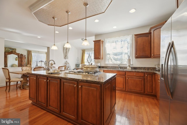 kitchen featuring light wood finished floors, dark stone counters, a kitchen island, decorative light fixtures, and stainless steel appliances