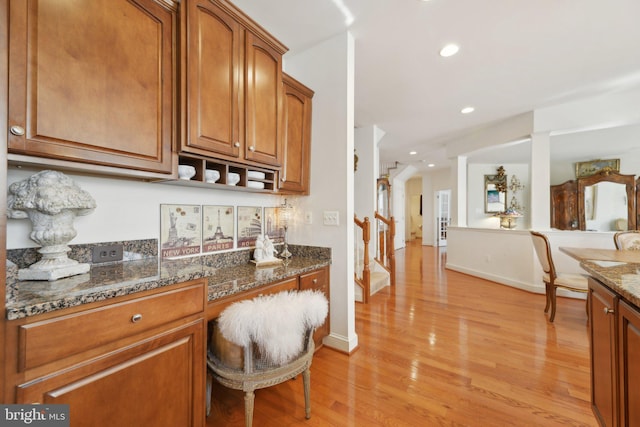 kitchen featuring light wood-type flooring, brown cabinetry, dark stone countertops, and recessed lighting