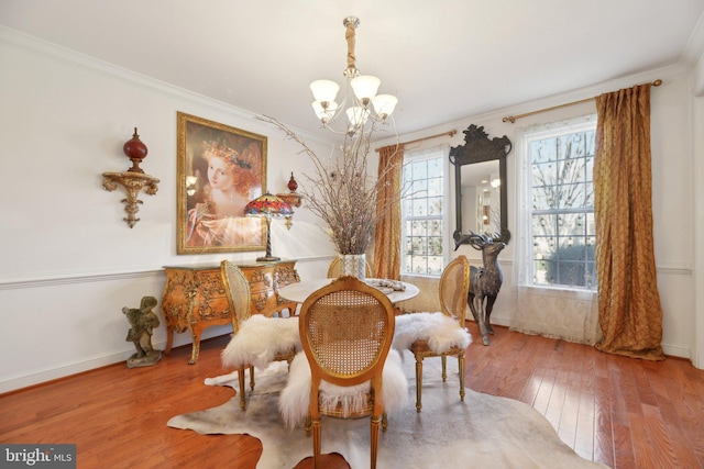 dining room with wood-type flooring, a notable chandelier, crown molding, and baseboards