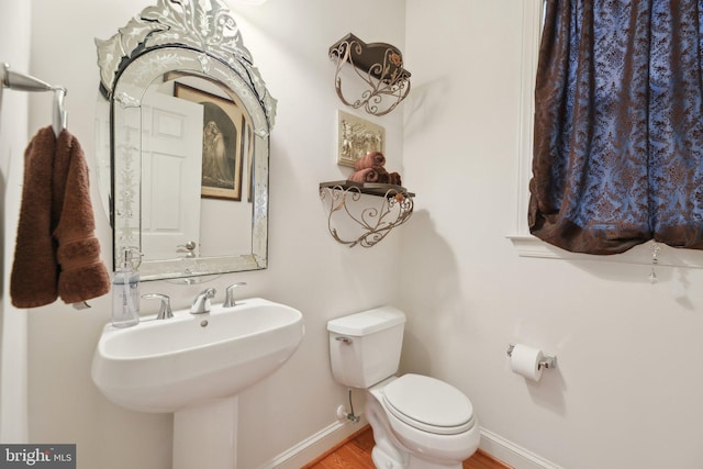 bathroom featuring toilet, a sink, baseboards, and wood finished floors