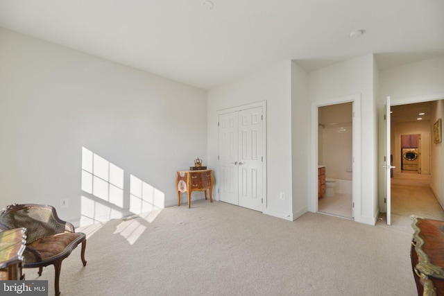 sitting room with washer / clothes dryer, light colored carpet, and baseboards