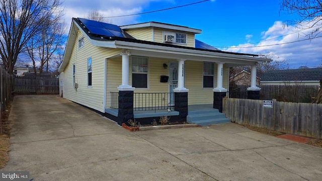 view of front of house featuring fence private yard, covered porch, roof mounted solar panels, and concrete driveway