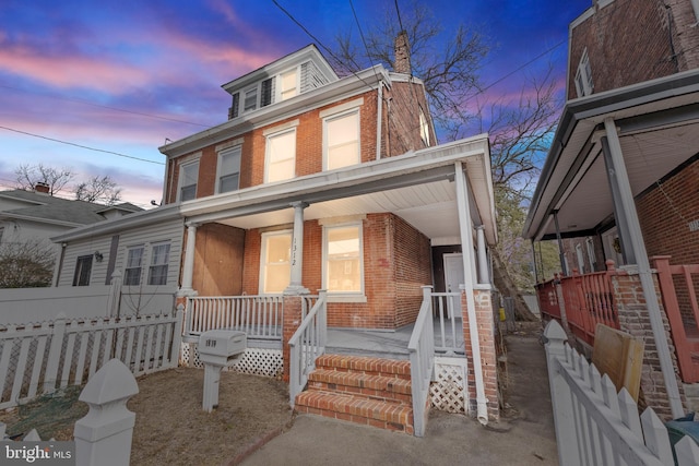 american foursquare style home with a porch, brick siding, and fence