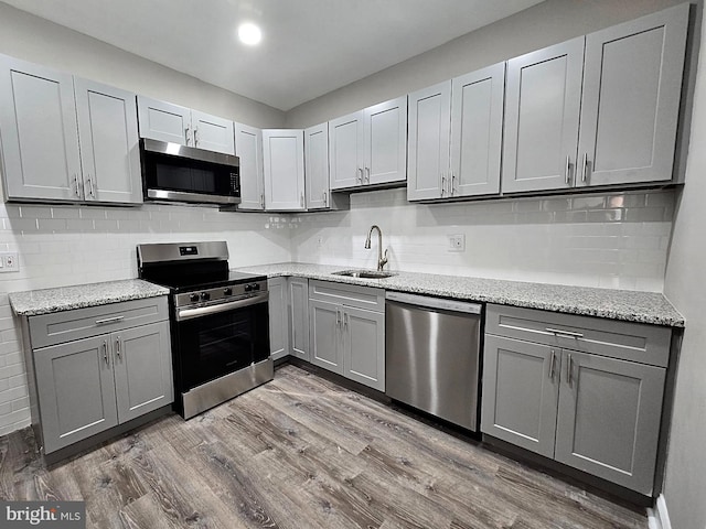 kitchen with light stone counters, wood finished floors, stainless steel appliances, gray cabinetry, and a sink