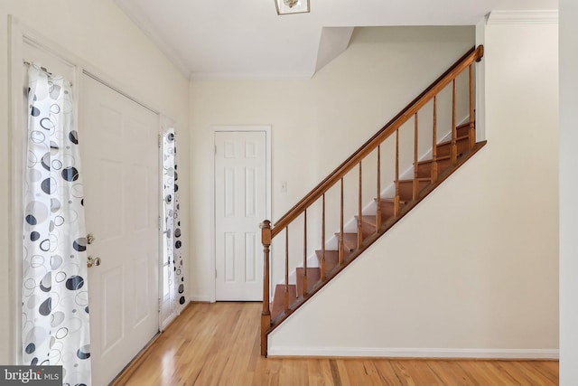 foyer entrance featuring baseboards, crown molding, stairway, and light wood finished floors