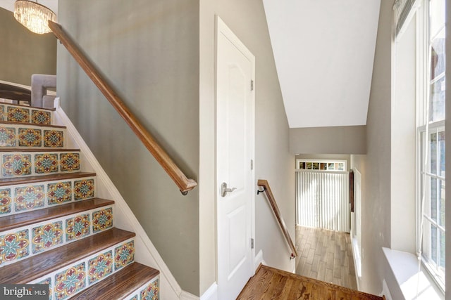 staircase with lofted ceiling, an inviting chandelier, and wood finished floors