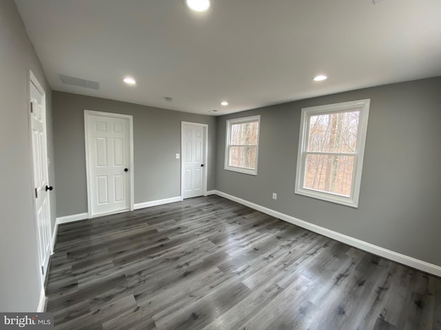 empty room with dark wood-style floors, recessed lighting, visible vents, and baseboards