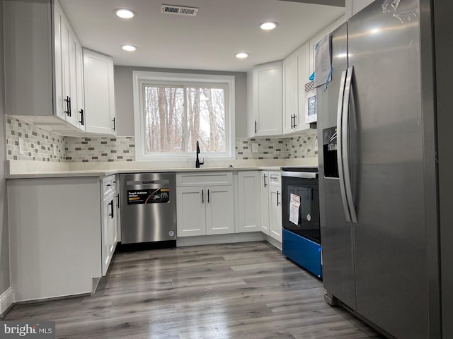 kitchen with light wood-style flooring, stainless steel appliances, a sink, white cabinets, and light countertops