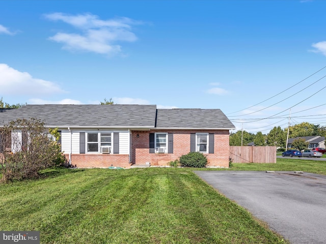 single story home with brick siding, a front yard, fence, and a shingled roof