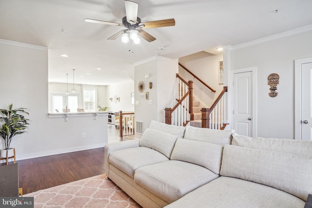 living area with wood finished floors, a ceiling fan, baseboards, ornamental molding, and stairway