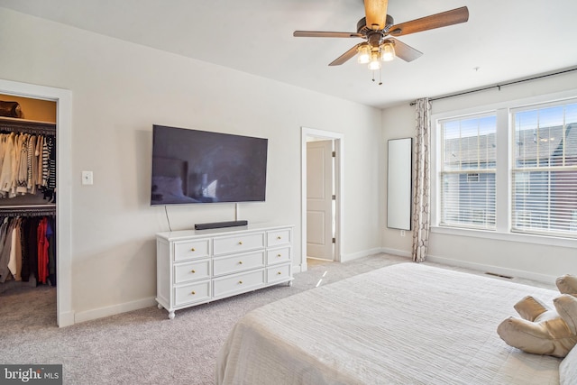 bedroom featuring light carpet, a closet, a walk in closet, and baseboards