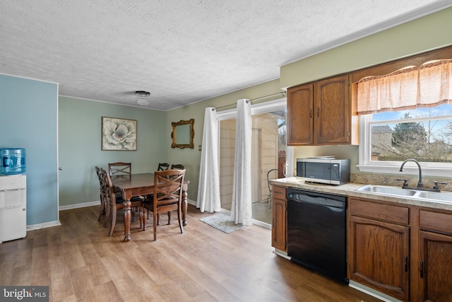 kitchen featuring brown cabinetry, dishwasher, stainless steel microwave, light countertops, and a sink