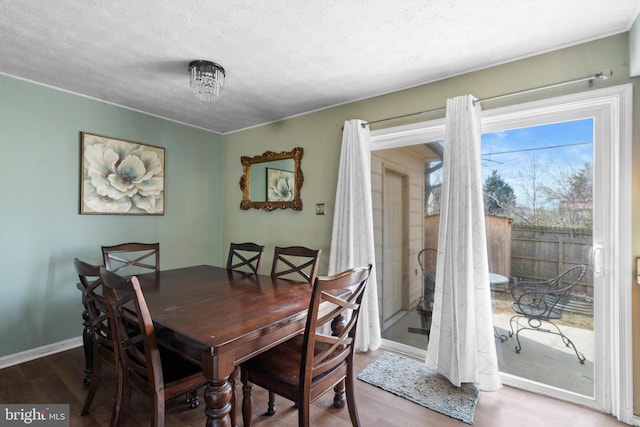 dining space with a textured ceiling, baseboards, and wood finished floors