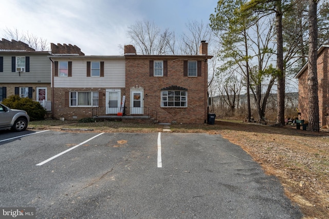 view of property featuring uncovered parking, brick siding, a chimney, and crawl space