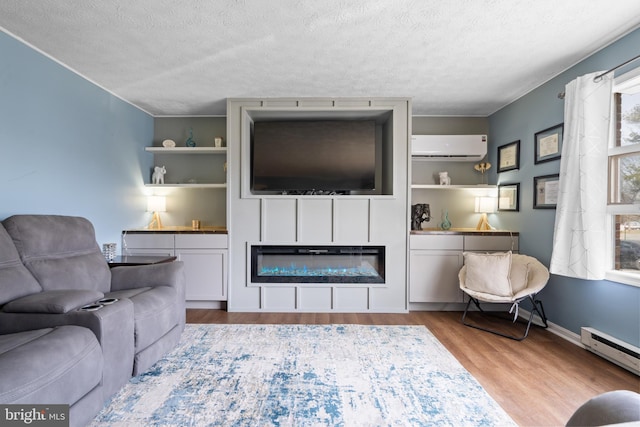 living area featuring a textured ceiling, baseboard heating, light wood-type flooring, a wall mounted air conditioner, and a glass covered fireplace