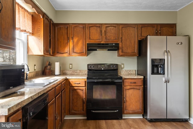 kitchen featuring black appliances, under cabinet range hood, light countertops, and brown cabinetry