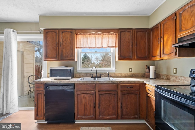 kitchen featuring under cabinet range hood, light countertops, a textured ceiling, black appliances, and a sink