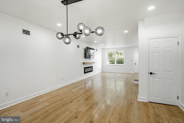 unfurnished living room featuring recessed lighting, visible vents, baseboards, light wood-style floors, and a glass covered fireplace