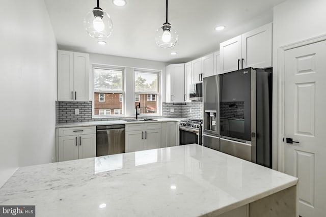 kitchen featuring light stone counters, hanging light fixtures, stainless steel appliances, white cabinetry, and a sink