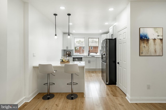 kitchen with pendant lighting, a breakfast bar area, light countertops, black fridge with ice dispenser, and white cabinets