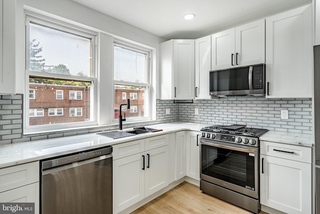 kitchen with stainless steel appliances, a sink, white cabinetry, and light stone countertops