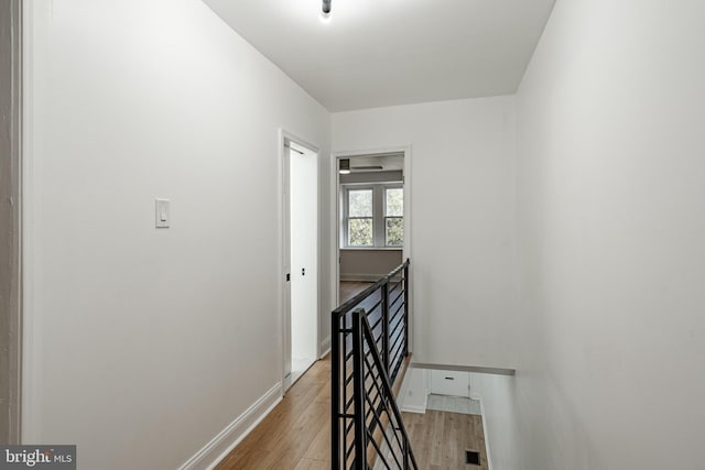 hallway with light wood-style flooring, visible vents, baseboards, and an upstairs landing