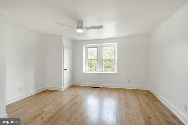 spare room featuring light wood finished floors, a ceiling fan, visible vents, and baseboards