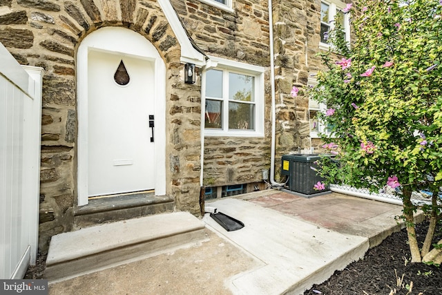 doorway to property with stone siding, a patio, and cooling unit