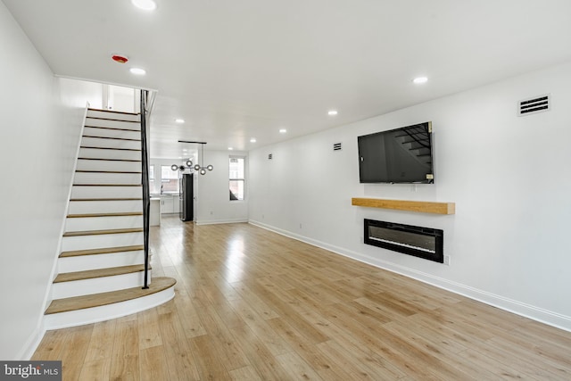 unfurnished living room with visible vents, a glass covered fireplace, light wood-style flooring, stairs, and recessed lighting