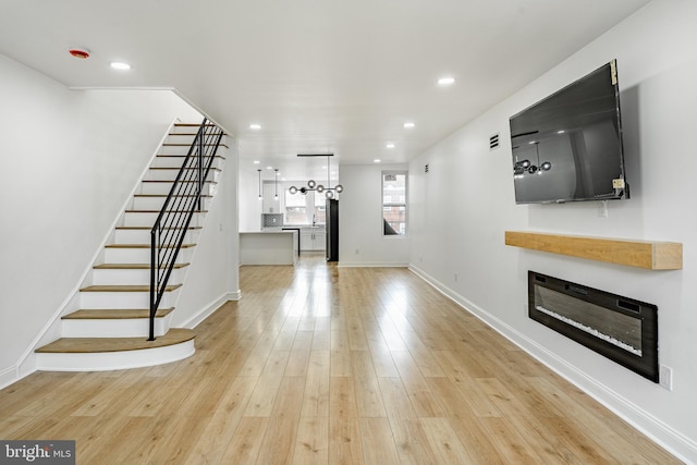 unfurnished living room featuring stairs, light wood finished floors, a glass covered fireplace, and recessed lighting