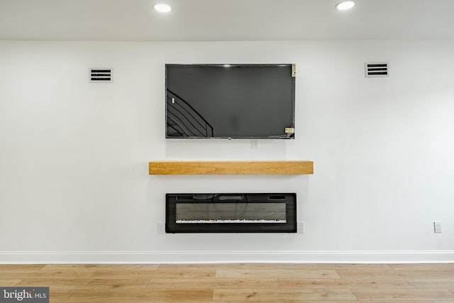 interior details with baseboards, visible vents, wood finished floors, and a glass covered fireplace