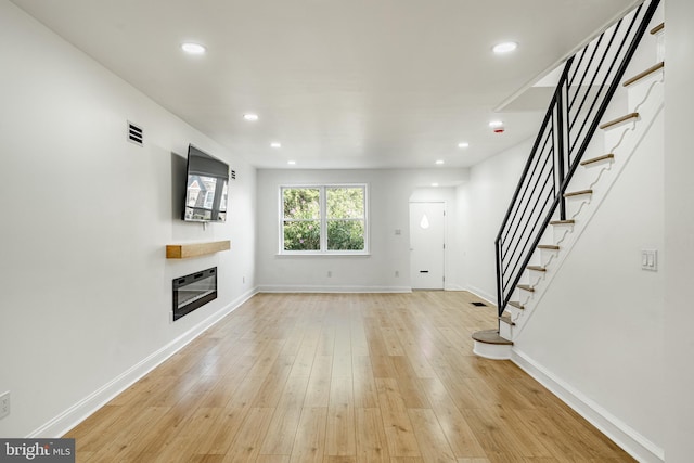 unfurnished living room with light wood finished floors, baseboards, a glass covered fireplace, stairway, and recessed lighting