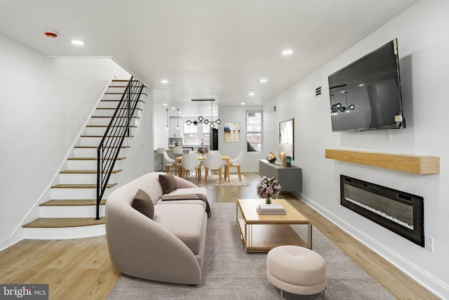 living room featuring recessed lighting, stairs, wood finished floors, and a glass covered fireplace