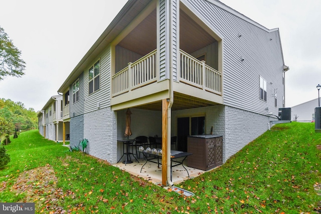 rear view of house featuring brick siding, a patio, a lawn, a balcony, and cooling unit