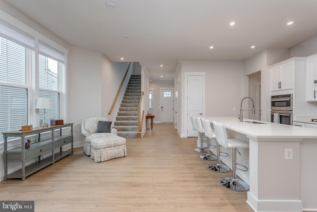 kitchen featuring light wood-style flooring, white cabinetry, a kitchen bar, double oven, and a sink